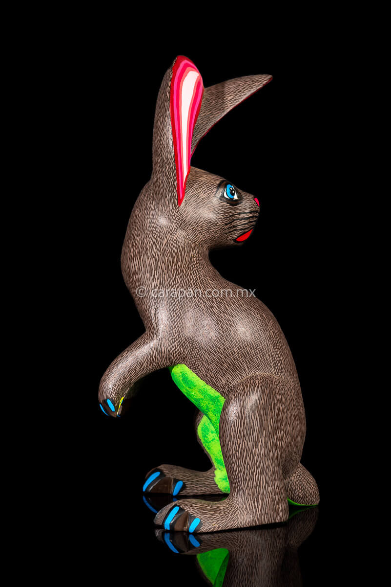 Mexican Wooden Sculpture of a gray Rabbit Looking Backwards with delicate black strokes that resemble hair & pink oranges It was carved from a single block of wood