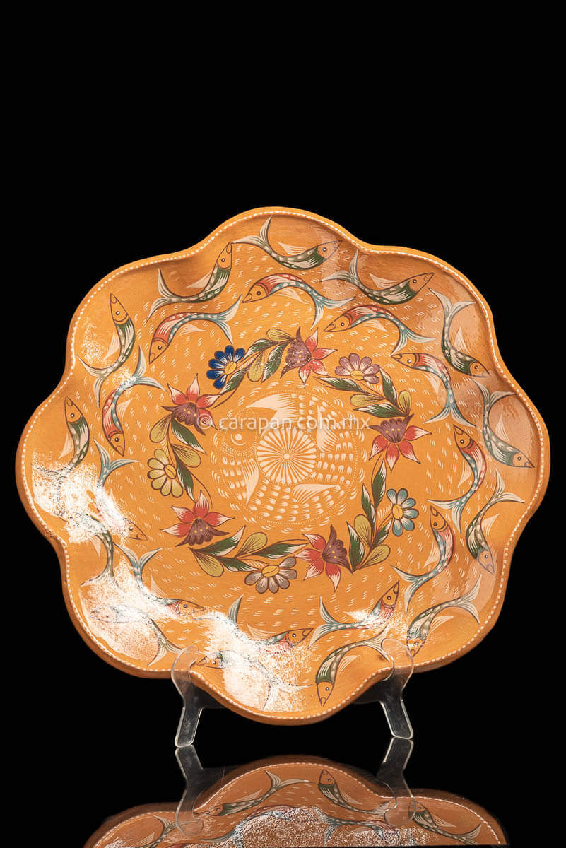 Light orange dish with curvy flower shape decorated with two circles of fishes painted in green and dark orange following by a circle of flowers and one  fish in beige at the center with its mouth near its tail in circular position. Finally, a star in beige with a white dot and strokesat the center