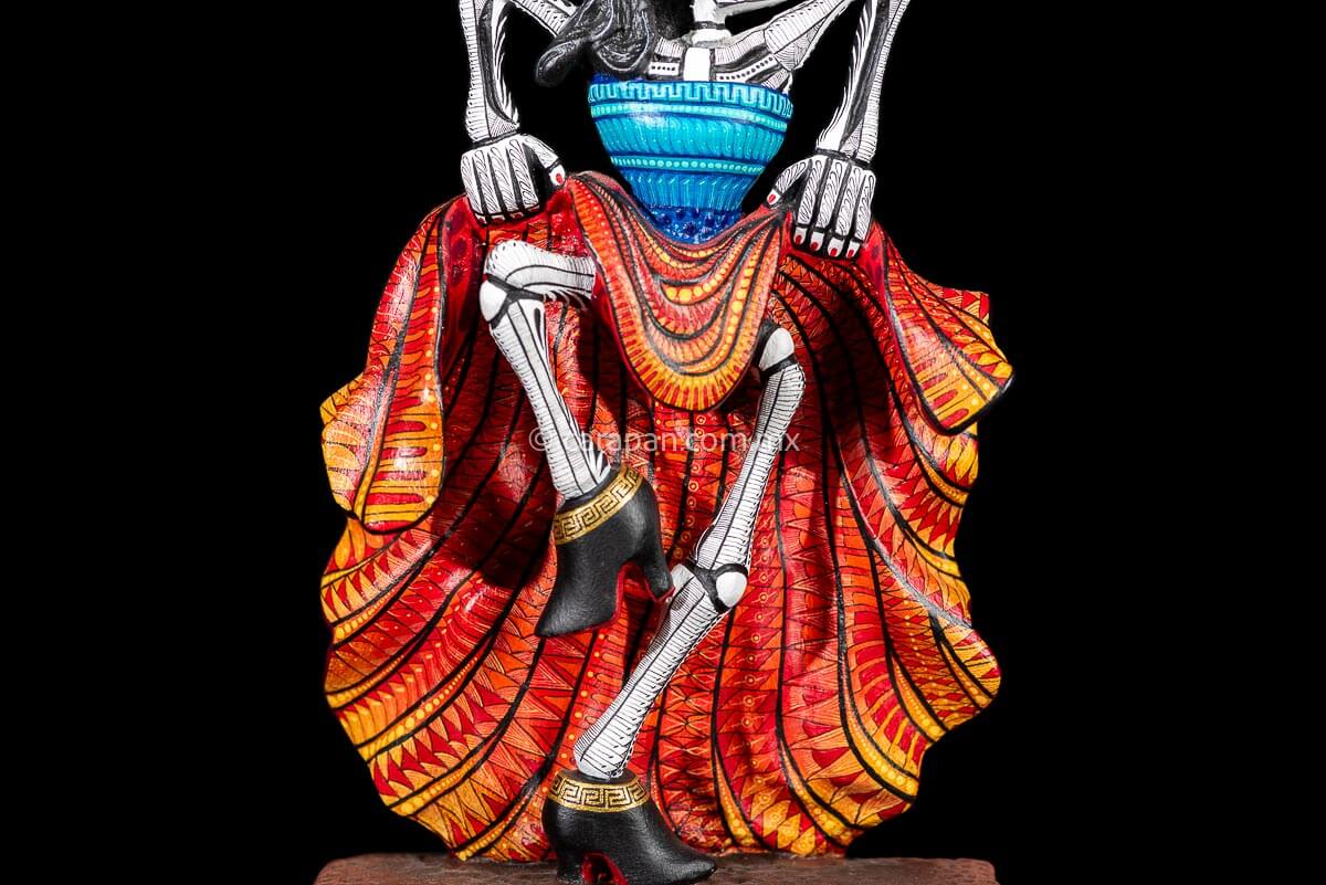 Day of the Dead Wooden Sculpture Mexican Catrina dancing can can lifting up her skirt she wears 3 feather haad dress, an orange skirt & a blue top her clothes are decoraated with zapotec symbols & the skeleton is meticulously decorated with patterns in black & White