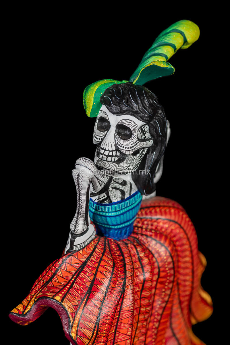 Day of the Dead Wooden Sculpture Mexican Catrina dancing can can lifting up her skirt she wears 3 feather haad dress, an orange skirt & a blue top her clothes are decoraated with zapotec symbols & the skeleton is meticulously decorated with patterns in black & White
