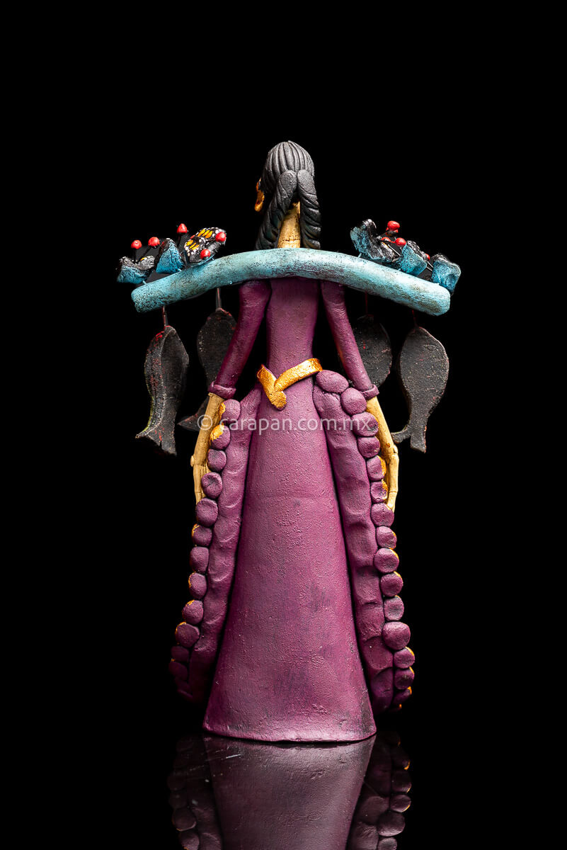 Mexican Clay Catrina carrying stick on her back with Fish and Butrerflies her skull is decorated with blue and red strokes and her dress has hand painted flowers back