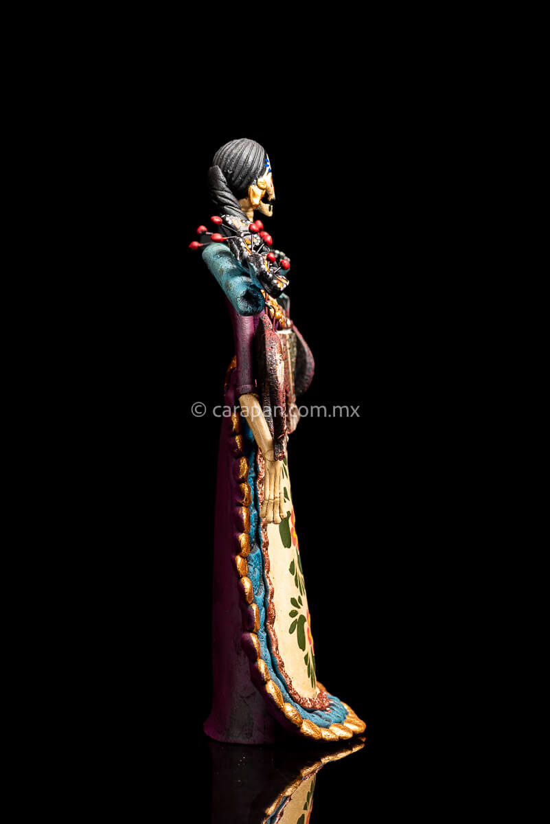 Mexican Clay Catrina carrying stick on her back with Fish and Butrerflies her skull is decorated with blue and red strokes and her dress has hand painted flowers side 1