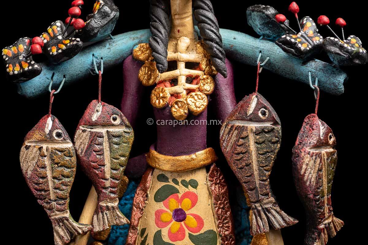 Mexican Clay Catrina carrying stick on her back with Fish and Butrerflies her skull is decorated with blue and red strokes and her dress has hand painted flowers