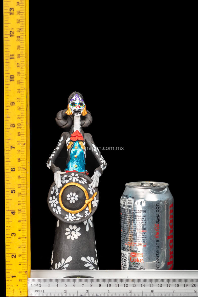 Catrina day of the dead Clay Sculpture dressed in a black and white charro dress  holding her hat on  her waist  with both hands.  Her skull is  hand painted.  Rulers