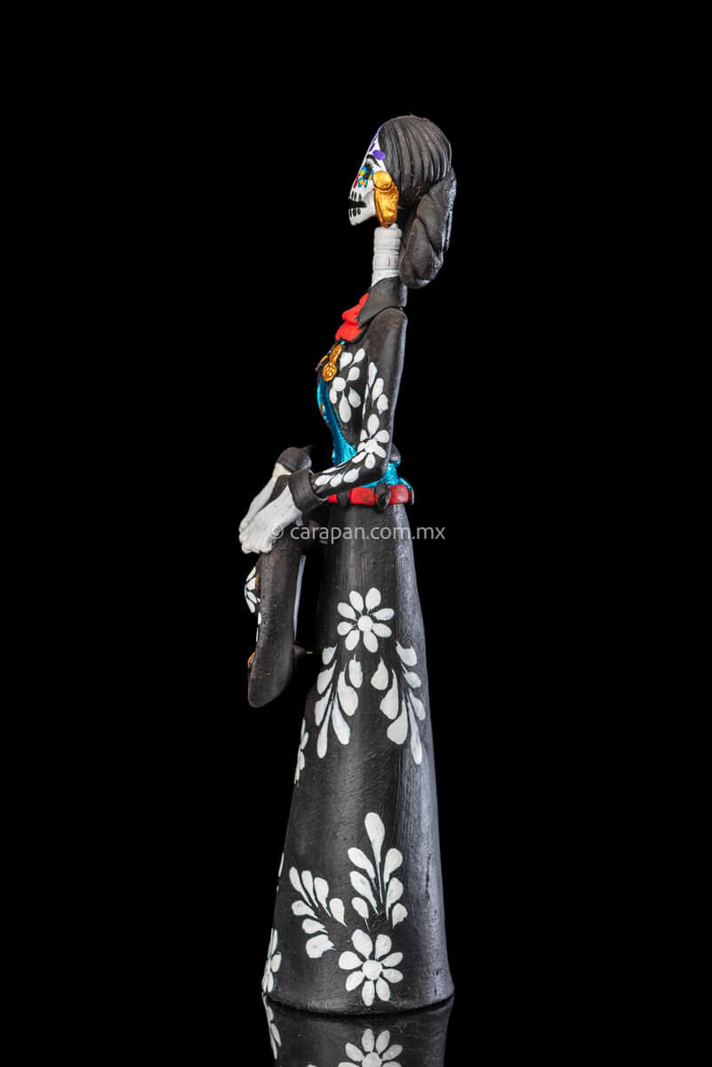 Catrina day of the dead Clay Sculpture dressed in a black and white charro dress  holding her hat on  her waist  with both hands.  Her skull is  hand painted.  Side