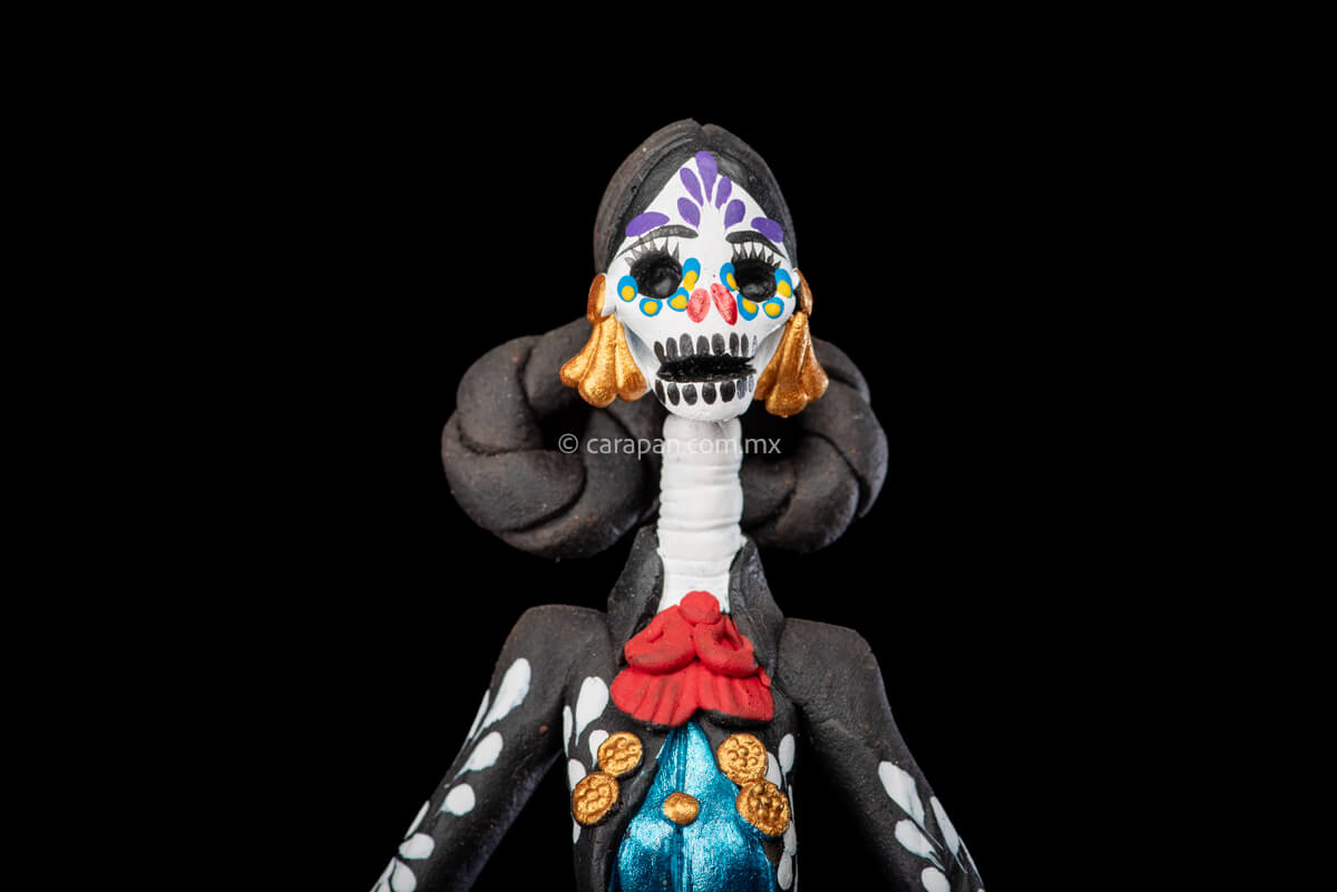 Catrina day of the dead Clay Sculpture dressed in a black and white charro dress  holding her hat on  her waist  with both hands.  Her skull is  hand painted.