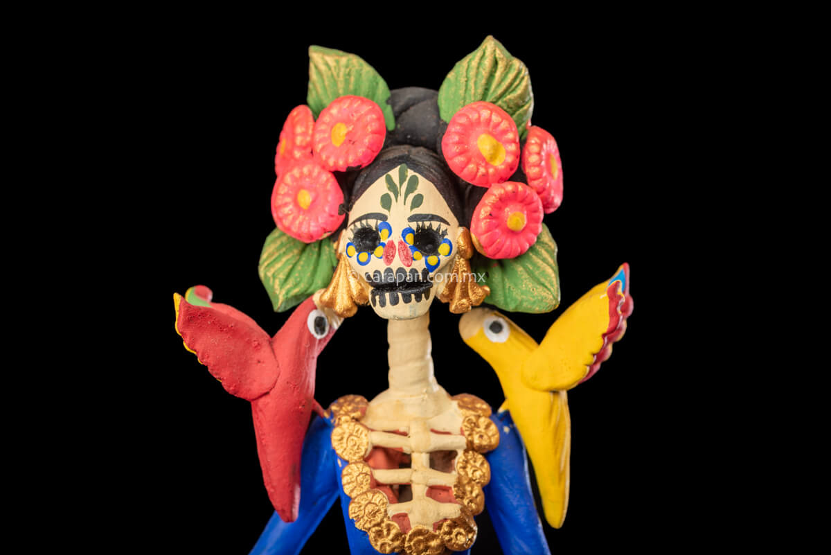 Mexican Clay Catrina Sculpture with blue dress and pink flowers. The catrina is inspired by Two of the most emblematic Frida Kahlo's self portraits with monkeys and parrots. Taht's why this catrina has three parrots and monkeys next to her. Her head dress is decorated with pink flowers and her skull is hand painted.
