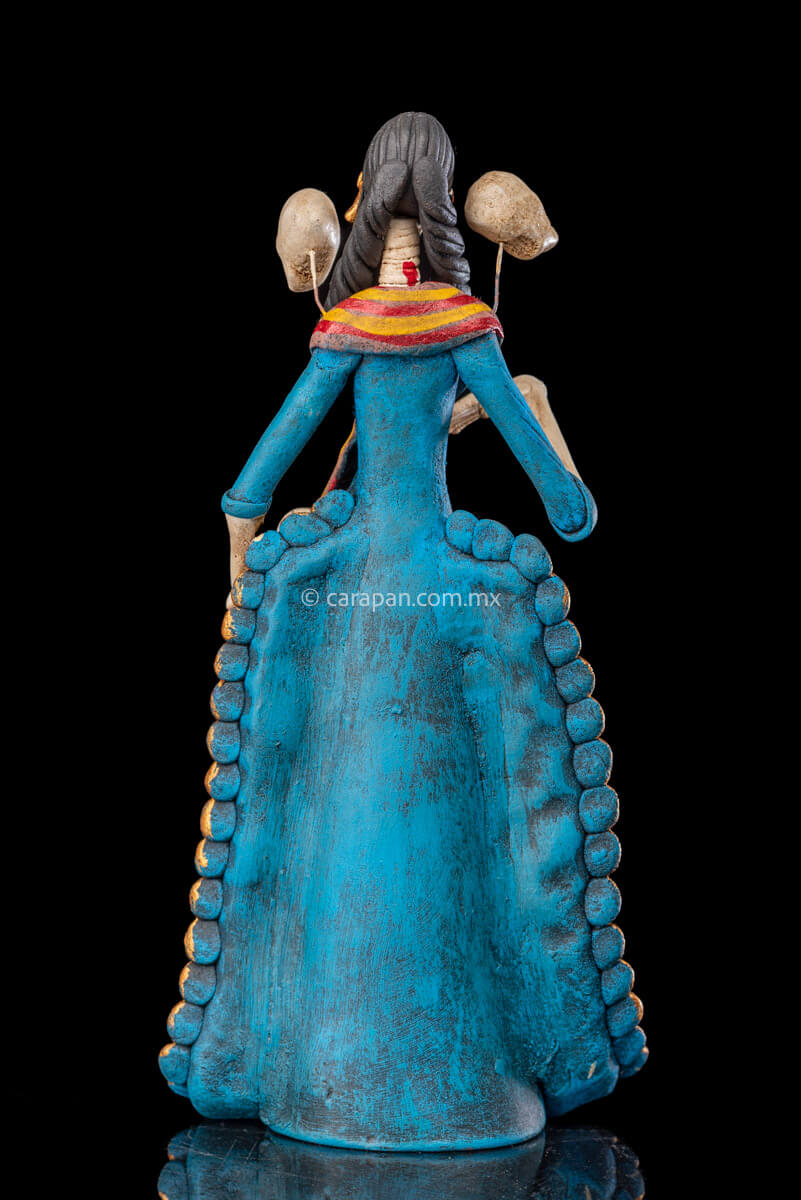 Catrina clay sculpture wearing a traditional Purépecha dress with a rebozo.  She carries 5 skulls in her rebozo and 4 more skulls adorn her dress. Two more skulls are next to her above each of her shoulders. Her dress is also decorated with pastillage flowers and painted flowers. Her own skull is hand painted in vibrant colors as well as her dress