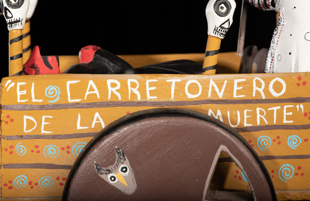 Cart pulled by a brown mule with 1 skeleton as rider & a figure representing the dead on it beside a death devil. The cart displays the legend in spanish that states "saving the world from evil" on one side & "Death's cart driver on the other side"
