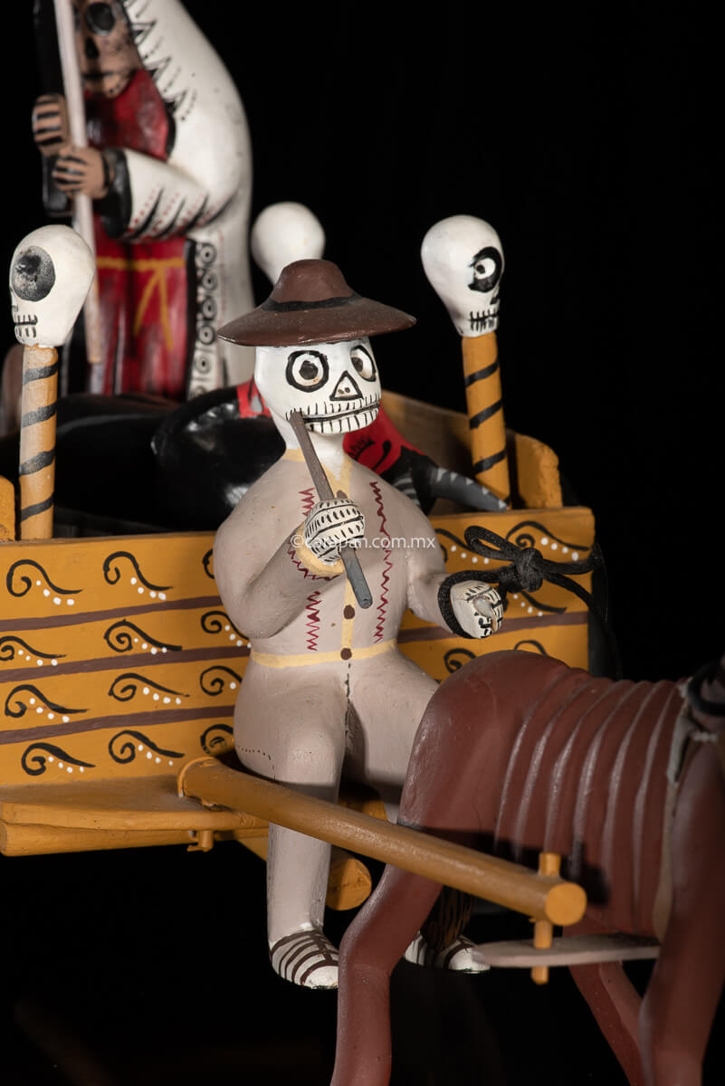 Cart pulled by a brown mule with 1 skeleton as rider & a figure representing the dead on it beside a death devil. The cart displays the legend in spanish that states "saving the world from evil" on one side & "Death's cart driver on the other side"