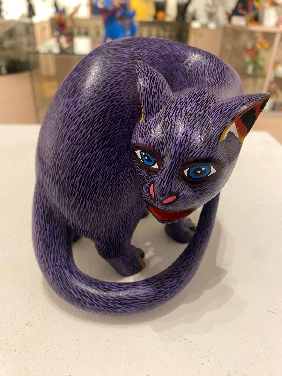 Mexican Wooden Sculpture of a purple cat looking backwards with delicate black strokes that resemble fur carved from a single block of wood