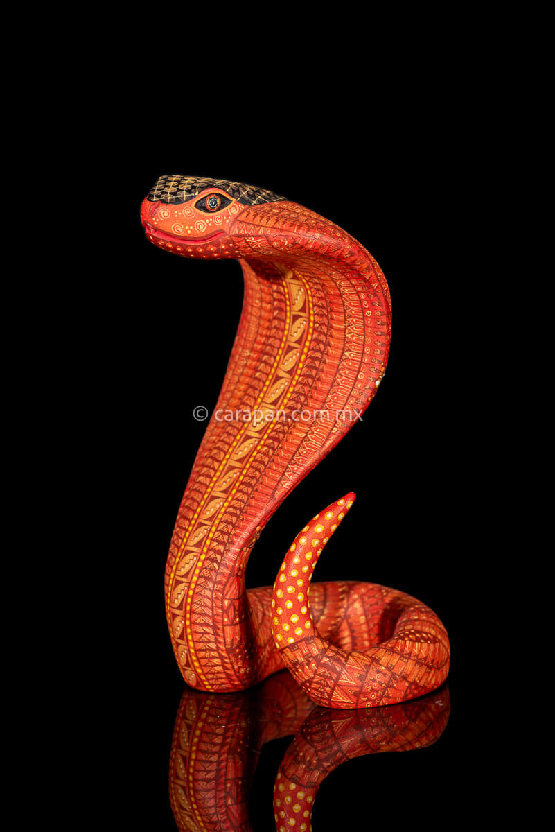 Wooden cobra hand carved from a single block of copal wood in Oaxaca Mexico, decorated with a fine pattern of zapotec symbols in a predominant orange tone