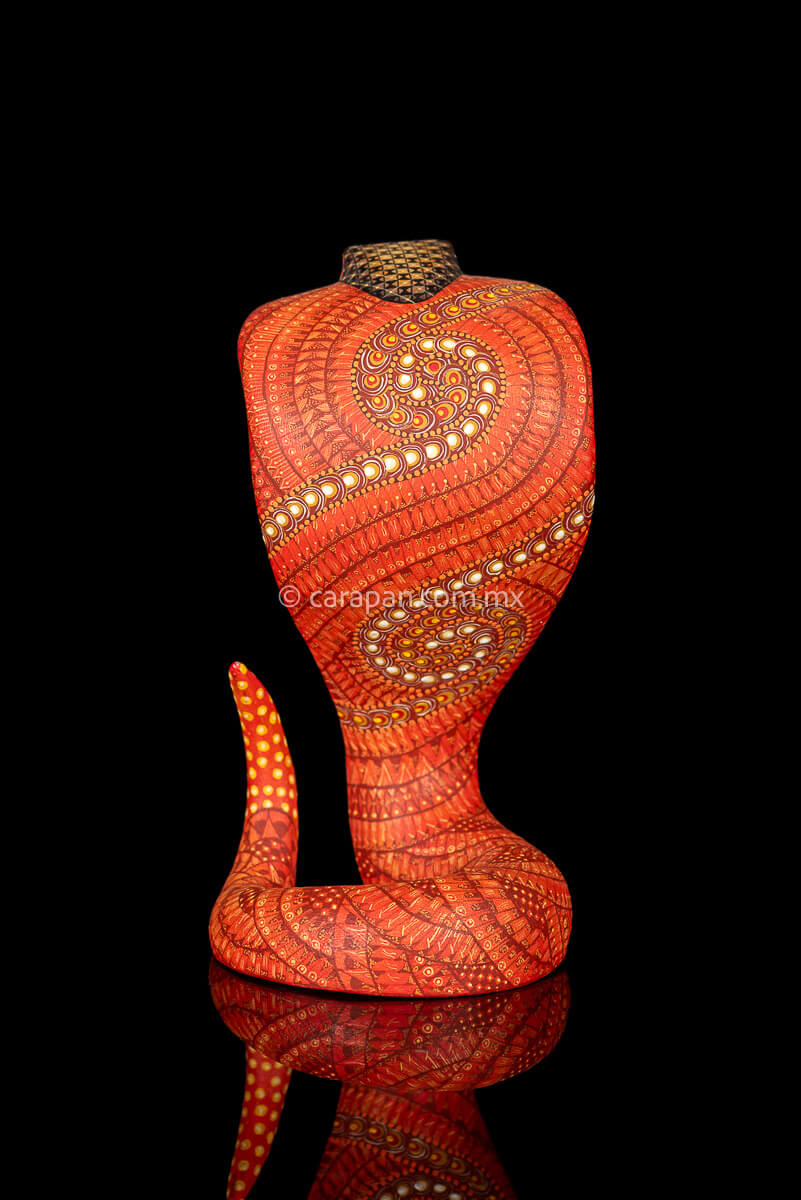 Wooden cobra hand carved from a single block of copal wood in Oaxaca Mexico, decorated with a fine pattern of zapotec symbols in a predominant orange tone 