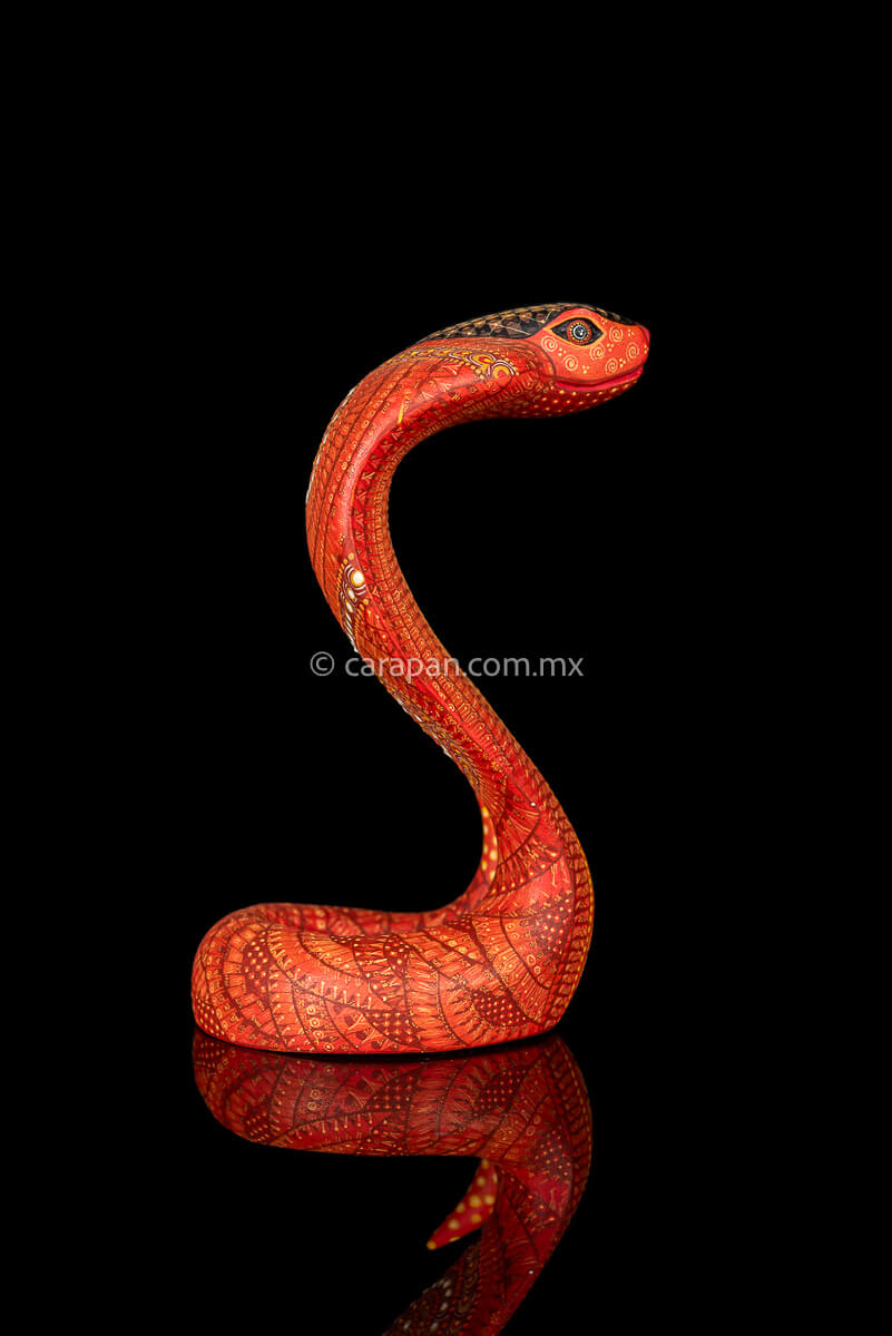 Wooden cobra hand carved from a single block of copal wood in Oaxaca Mexico, decorated with a fine pattern of zapotec symbols in a predominant orange tone 