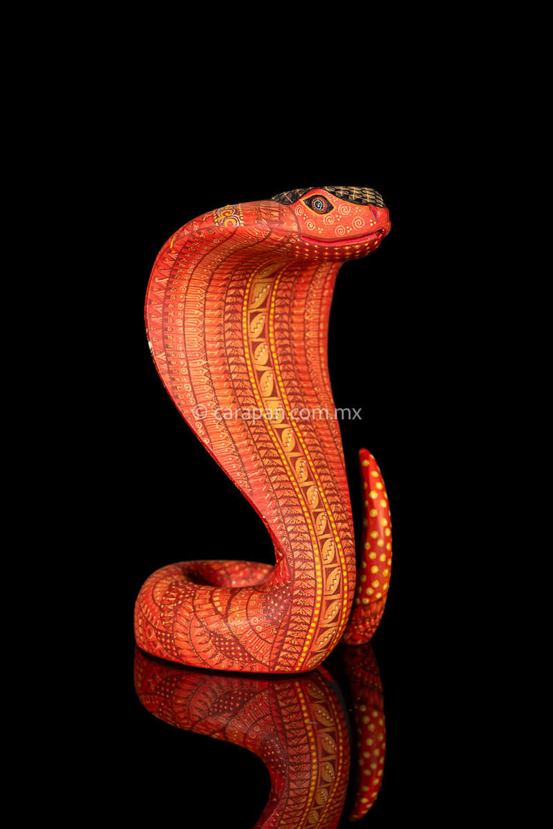 Wooden cobra hand carved from a single block of copal wood in Oaxaca Mexico, decorated with a fine pattern of zapotec symbols in a predominant orange tone 