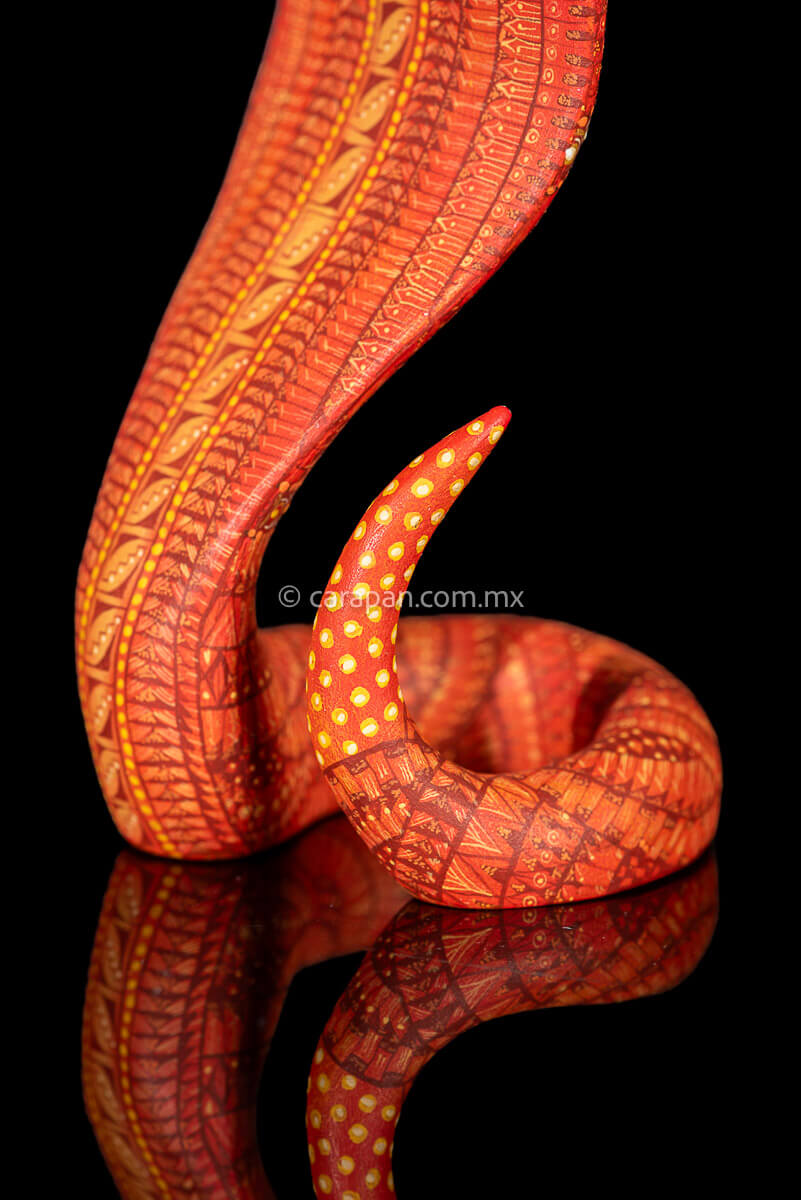 Wooden cobra hand carved from a single block of copal wood in Oaxaca Mexico, decorated with a fine pattern of zapotec symbols in a predominant orange tone 