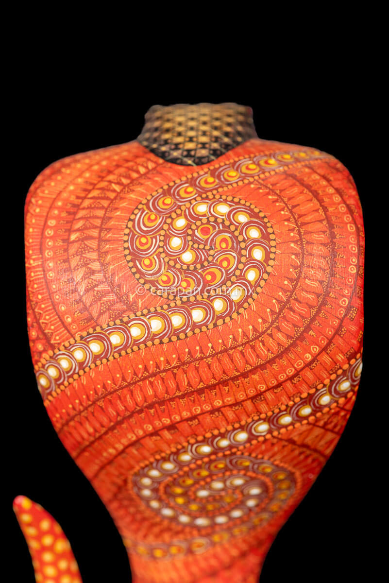 Wooden cobra hand carved from a single block of copal wood in Oaxaca Mexico, decorated with a fine pattern of zapotec symbols in a predominant orange tone 