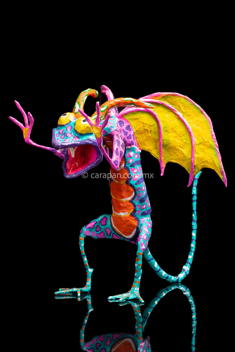 User  Please create a selling description for Paper Mache Alebrije Dragon Style Standing with hands up and mouth open showing 2 fangs popping yellow eyes and two orange horns. His body is painted in turquoise with pink dots and blue stripes and his wings are yellow outlined in pink