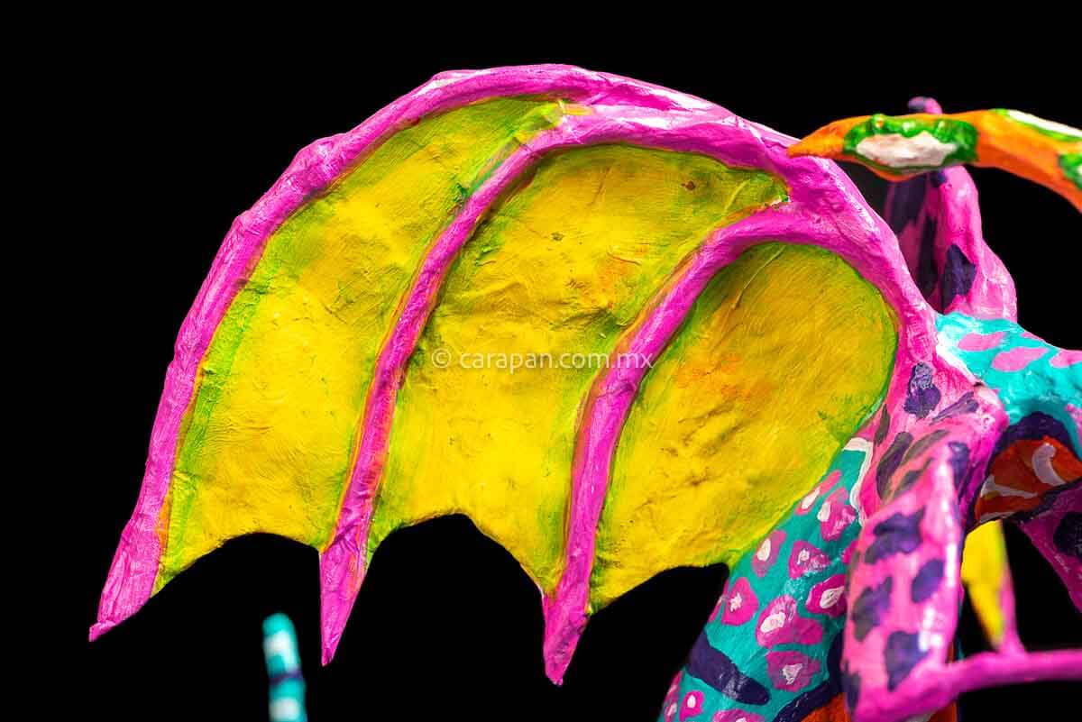 User  Please create a selling description for Paper Mache Alebrije Dragon Style Standing with hands up and mouth open showing 2 fangs popping yellow eyes and two orange horns. His body is painted in turquoise with pink dots and blue stripes and his wings are yellow outlined in pink