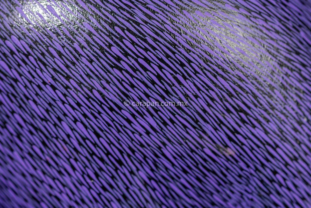 Detail of Mexican Wooden Sculpture of a purple cat looking backwards with delicate black strokes that resemble fur carved from a single block of wood