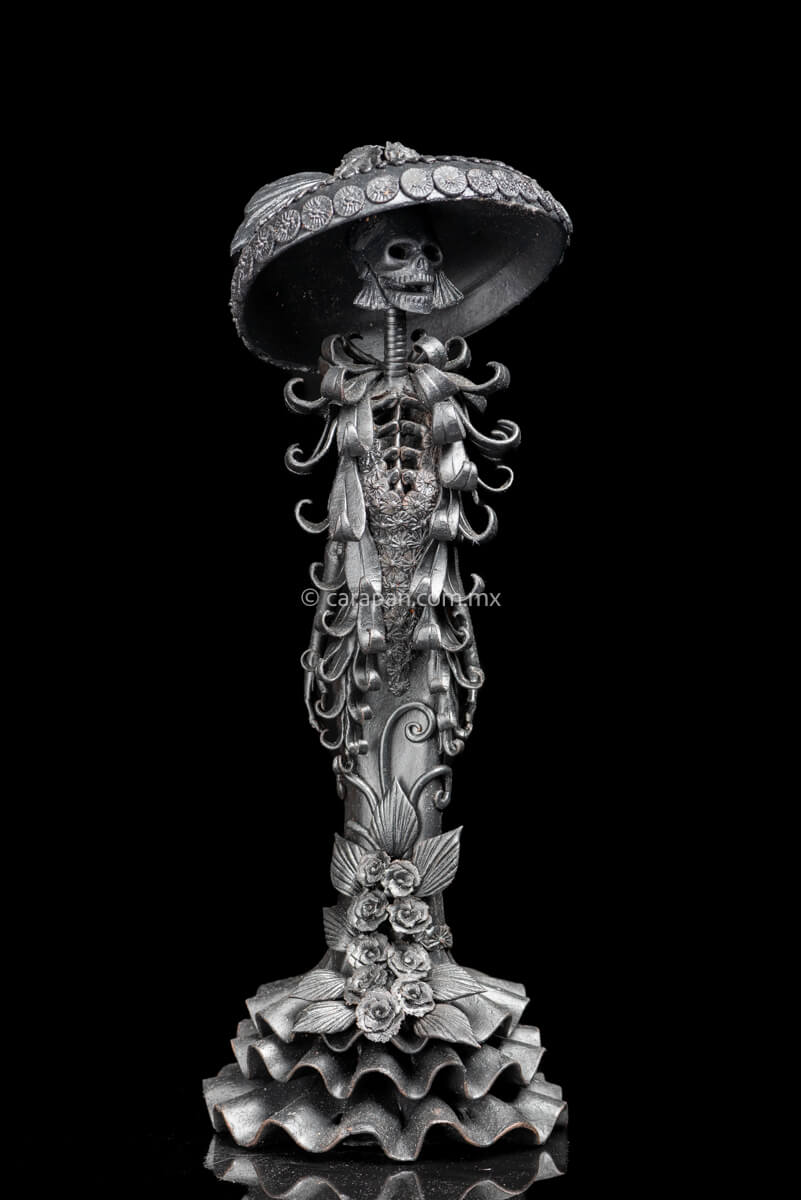  Catrina Sculpture in Black Inspired by José Guadalupe Posada's Catrina.  The sculpture is standing with both hands on her sides. Wearing a dress and a big hat decorated with vegetal motifs crafted with pastillage technique.  Her skull face is smiling. Crafted in Capula, Michoacan. 