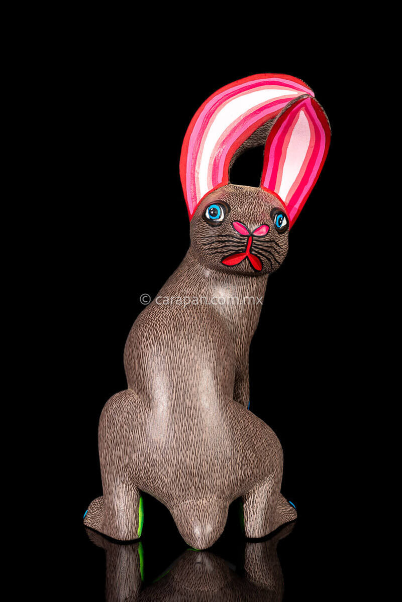 Mexican Wooden Sculpture of a gray Rabbit Looking Backwards with delicate black strokes that resemble hair & pink oranges It was carved from a single block of wood