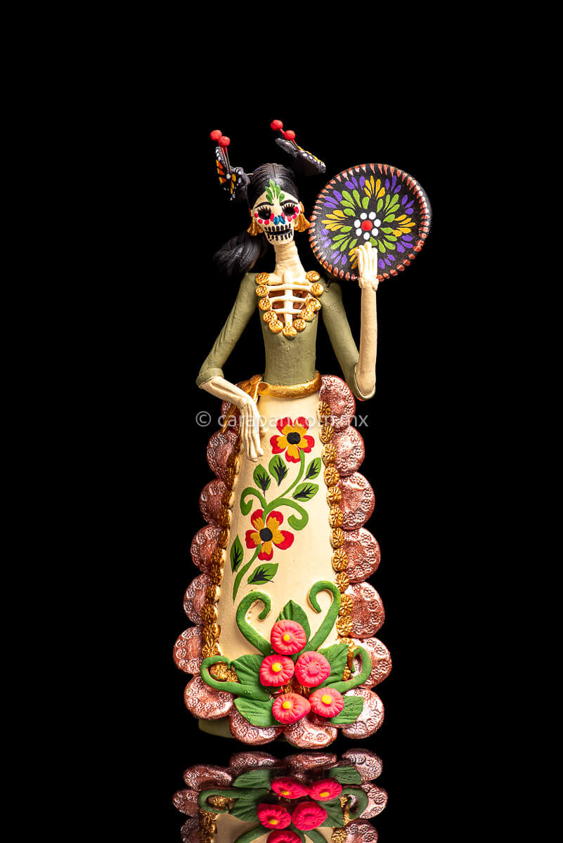 Colorful Mexican  Clay Catrina holding dish on her left hand with butterflies head dress and flowery dress 