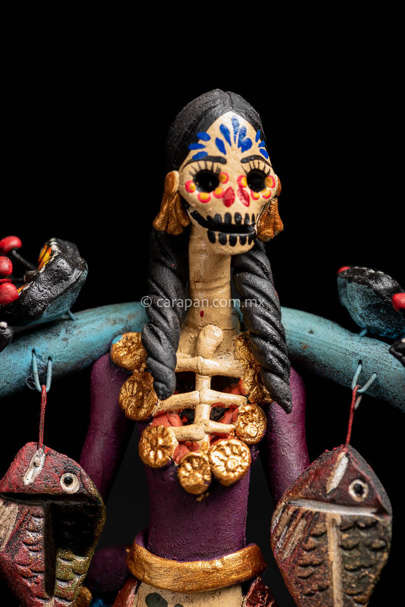 Mexican Clay Catrina carrying stick on her back with Fish and Butrerflies her skull is decorated with blue and red strokes and her dress has hand painted flowers