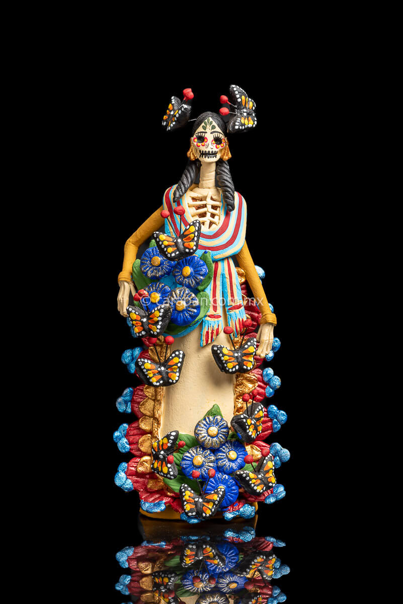 Mexican catrina with monarch butterflies her forehead is painted with green strokes and her eyes with yellow petals with red contour she also carries a rebozo around her neck