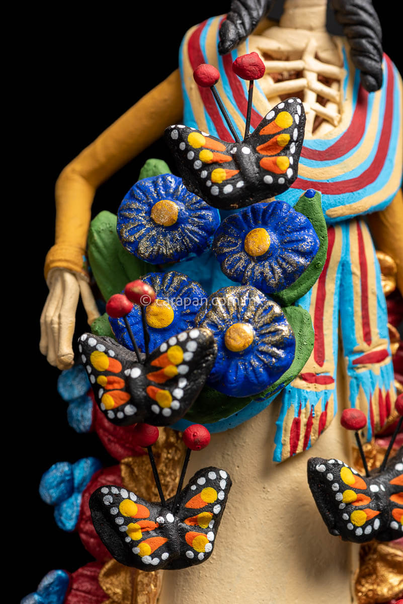 Mexican catrina with monarch butterflies her forehead is painted with green strokes and her eyes with yellow petals with red contour she also carries a rebozo around her neck butterflies detail