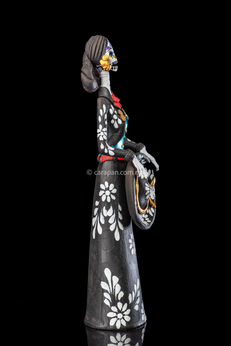 Catrina day of the dead Clay Sculpture dressed in a black and white charro dress  holding her hat on  her waist  with both hands.  Her skull is  hand painted.  side 2