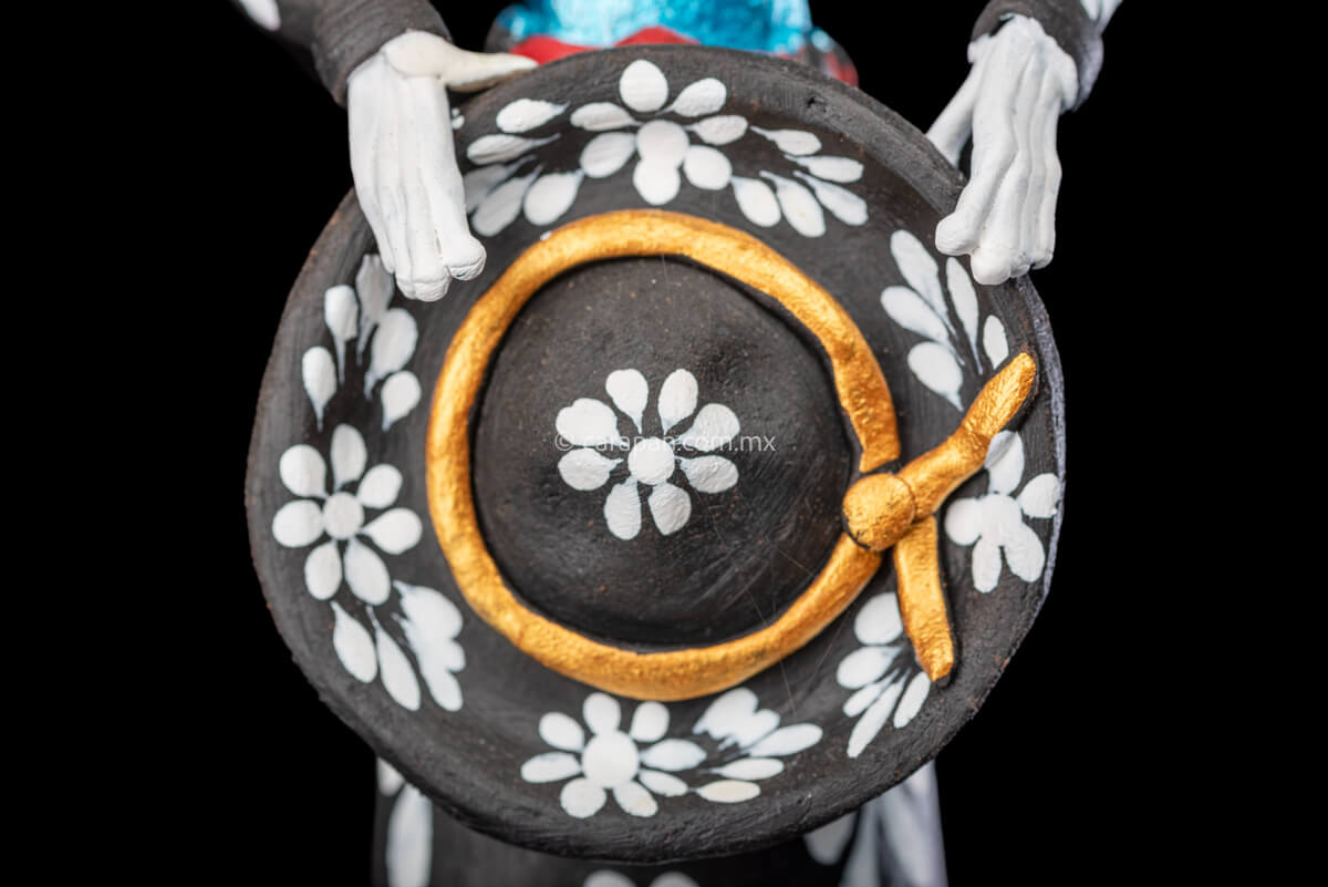 Catrina day of the dead Clay Sculpture dressed in a black and white charro dress  holding her hat on  her waist  with both hands.  Her skull is  hand painted.  hat