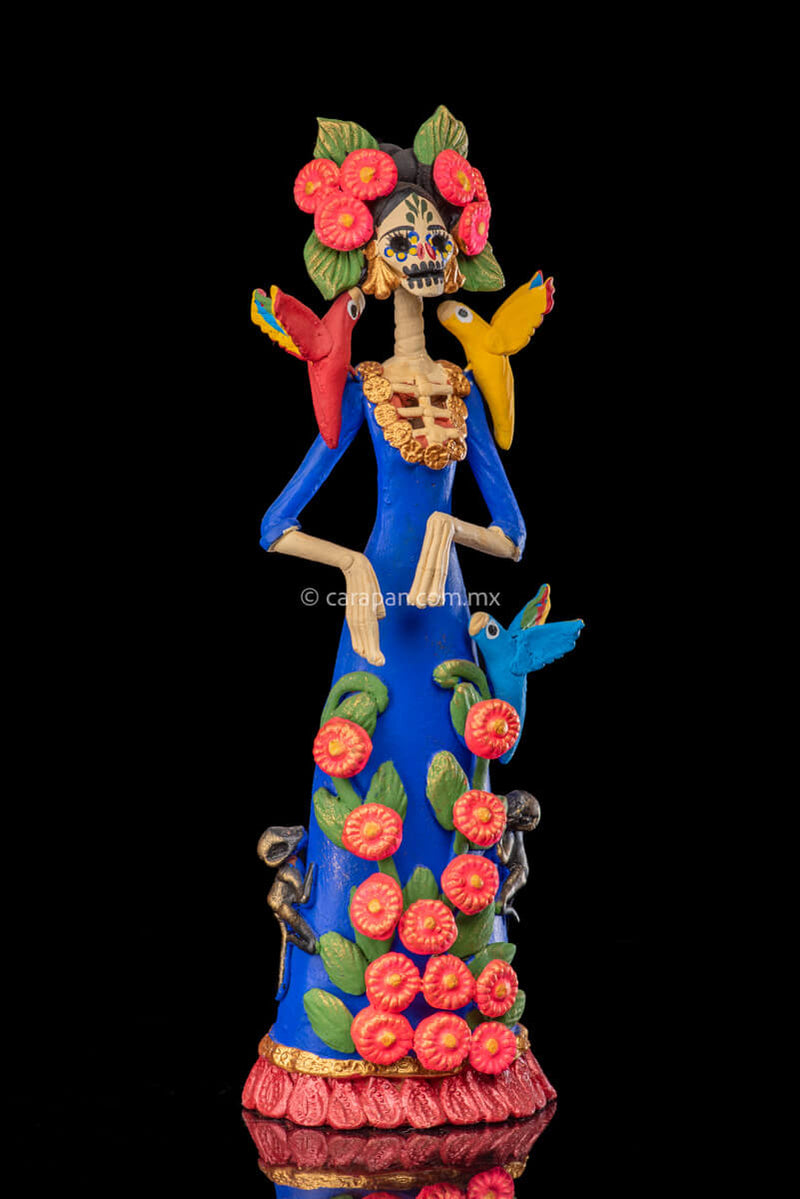 Mexican Clay Catrina Sculpture with blue dress and pink flowers. The catrina is inspired by Two of the most emblematic Frida Kahlo's self portraits with monkeys and parrots. Taht's why this catrina has three parrots and monkeys next to her. Her head dress is decorated with pink flowers and her skull is hand painted.