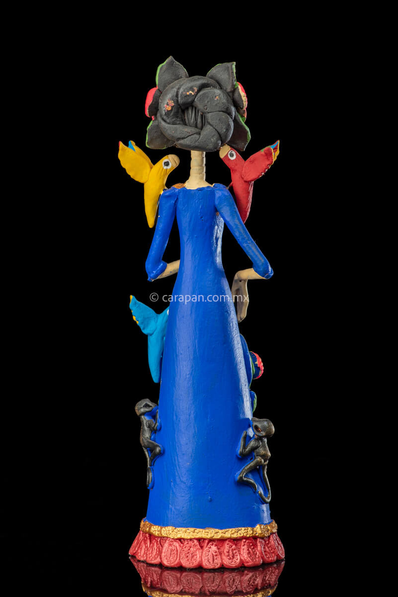 Mexican Clay Catrina Sculpture with blue dress and pink flowers. The catrina is inspired by Two of the most emblematic Frida Kahlo's self portraits with monkeys and parrots. Taht's why this catrina has three parrots and monkeys next to her. Her head dress is decorated with pink flowers and her skull is hand painted. back