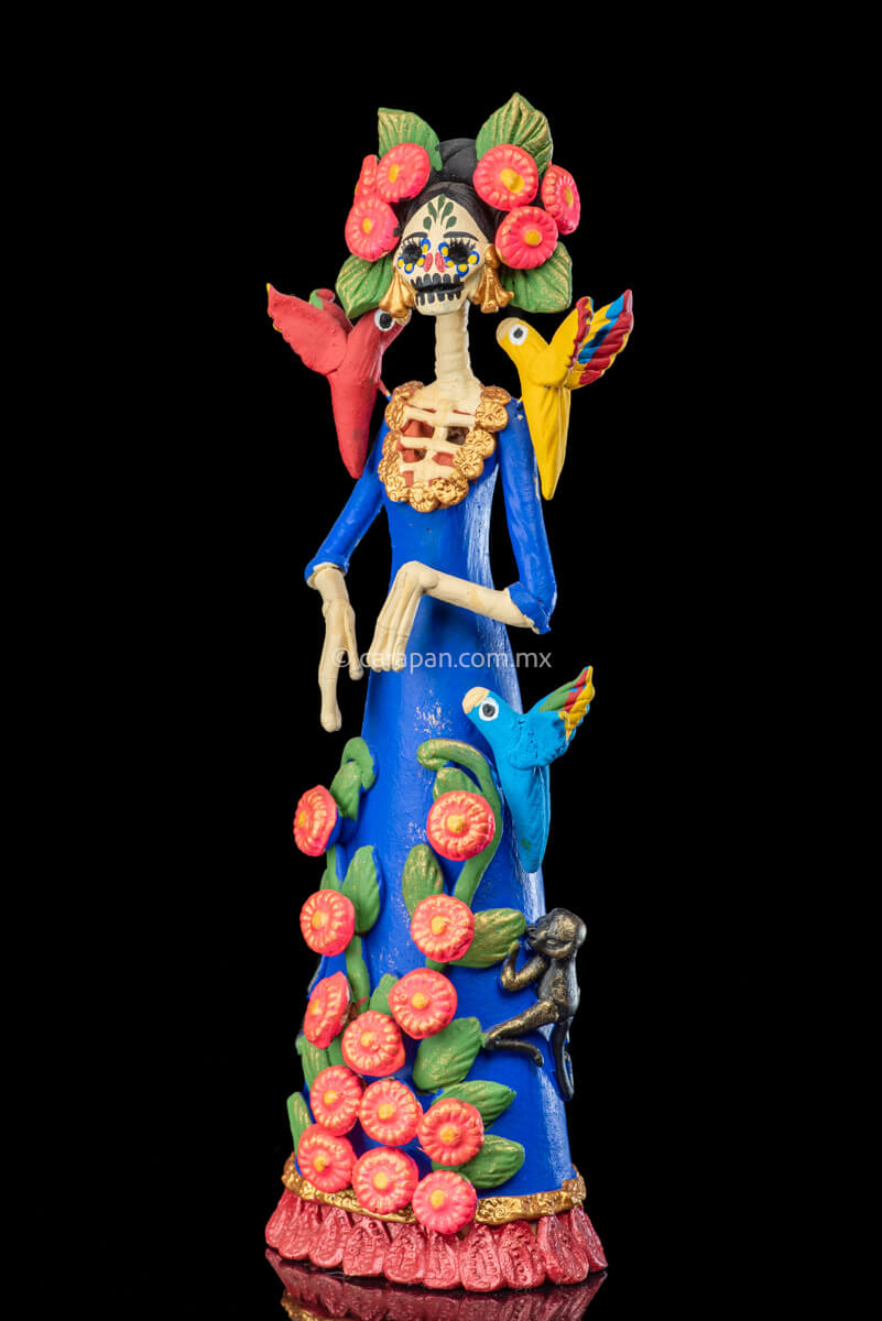 Mexican Clay Catrina Sculpture with blue dress and pink flowers. The catrina is inspired by Two of the most emblematic Frida Kahlo's self portraits with monkeys and parrots. Taht's why this catrina has three parrots and monkeys next to her. Her head dress is decorated with pink flowers and her skull is hand painted.