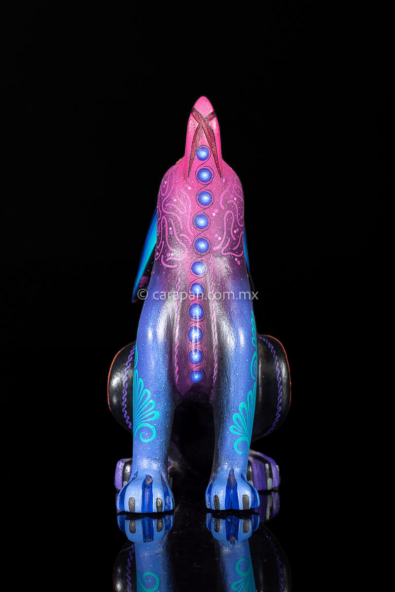 Wood carving of a Coyote looking up its body has blue, black and purple hues and is decorated with flowers and dots that resemble the stars