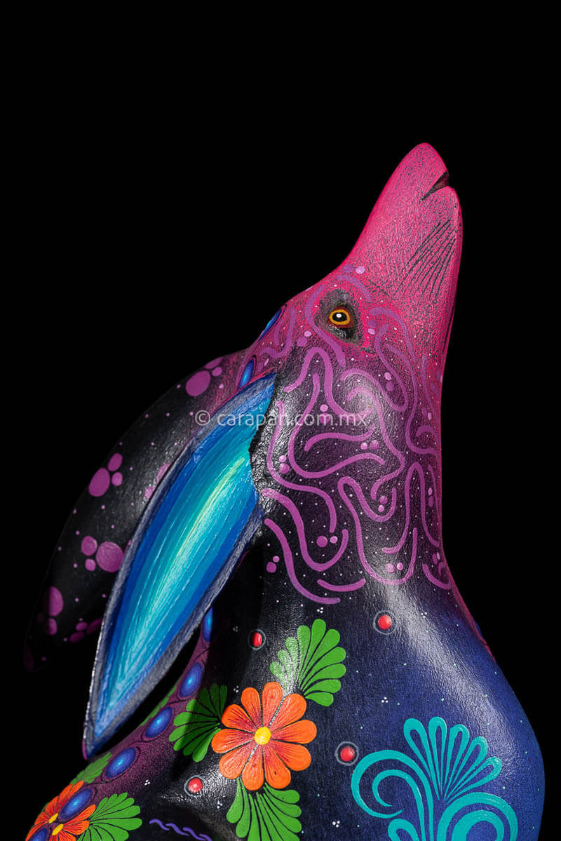 Head of Wood carving of a Coyote looking up its body has blue, black and purple hues and is decorated with flowers and dots that resemble the stars