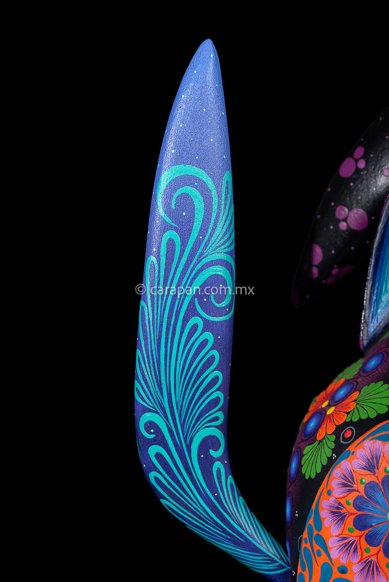 Tail of Wood carving of a Coyote looking up its body has blue, black and purple hues and is decorated with flowers and dots that resemble the stars