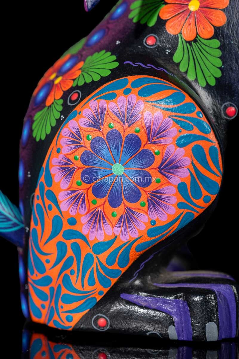 Leg of Wood carving of a Coyote looking up its body has blue, black and purple hues and is decorated with flowers and dots that resemble the stars
