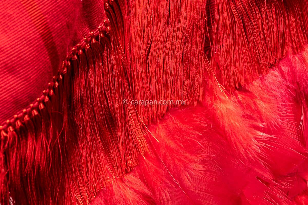 Detail of Backstrap loomed open poncho in red with feathered fringe. 