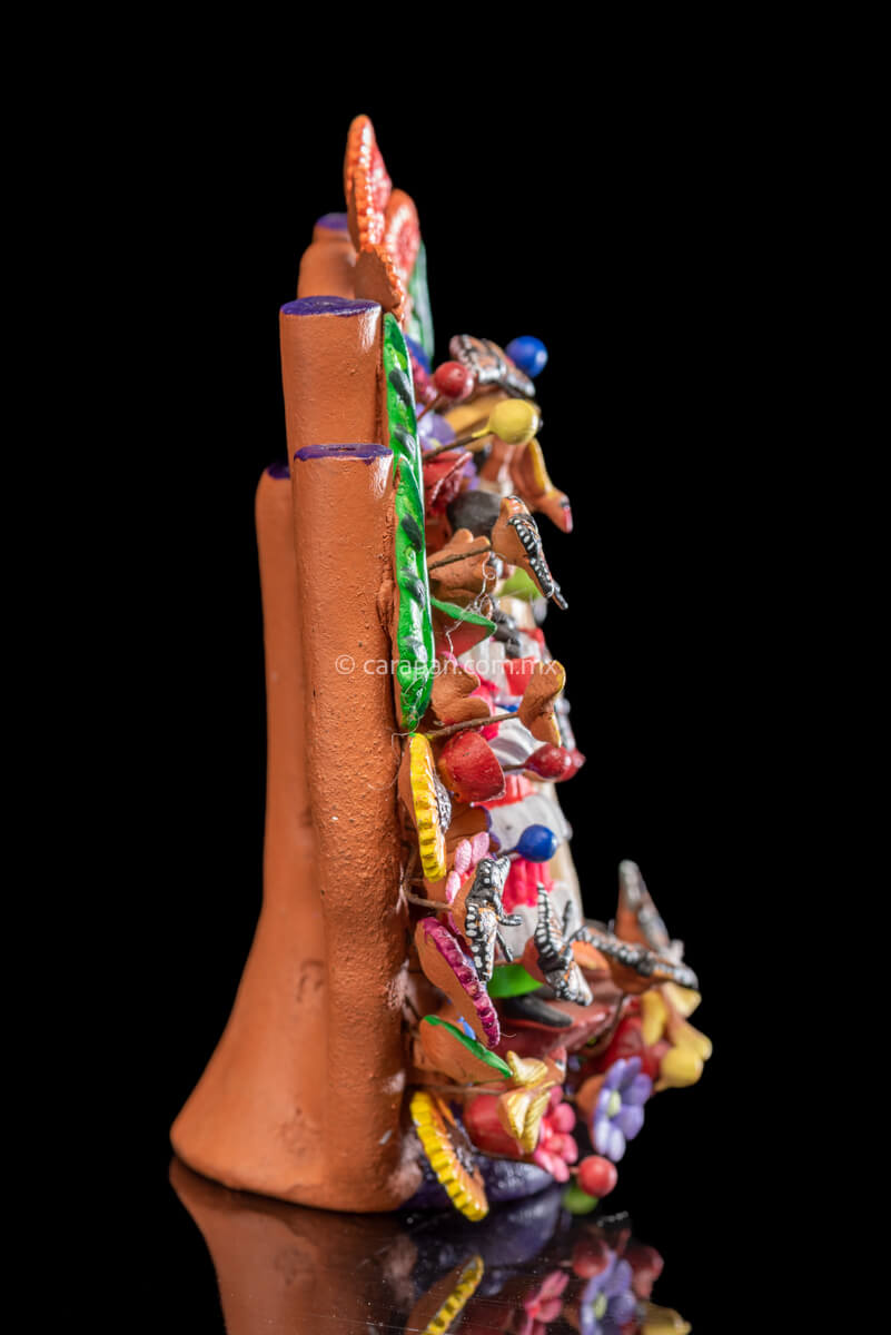Small Mexican Clay tree of life with Mazahua indigenous couple at the center surrounded by flowers and butterflies. The man wears a traditional costume in beig, hat and a bag. The woman wears a traditional dress in pink, orange and green with a blue belt.  Side 2