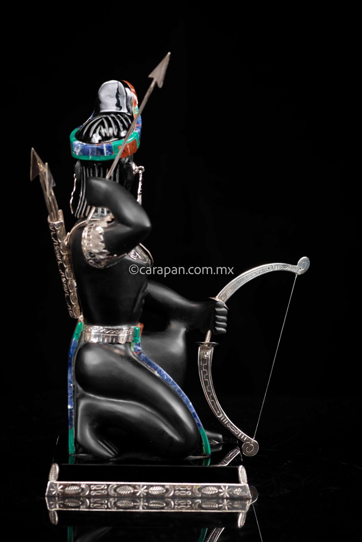 Obsidian Sculpture of Aztec Warrior with Bow & Arrows he is wearing two silver earrings, a silver necklace and two  silver sleeves with feathers
