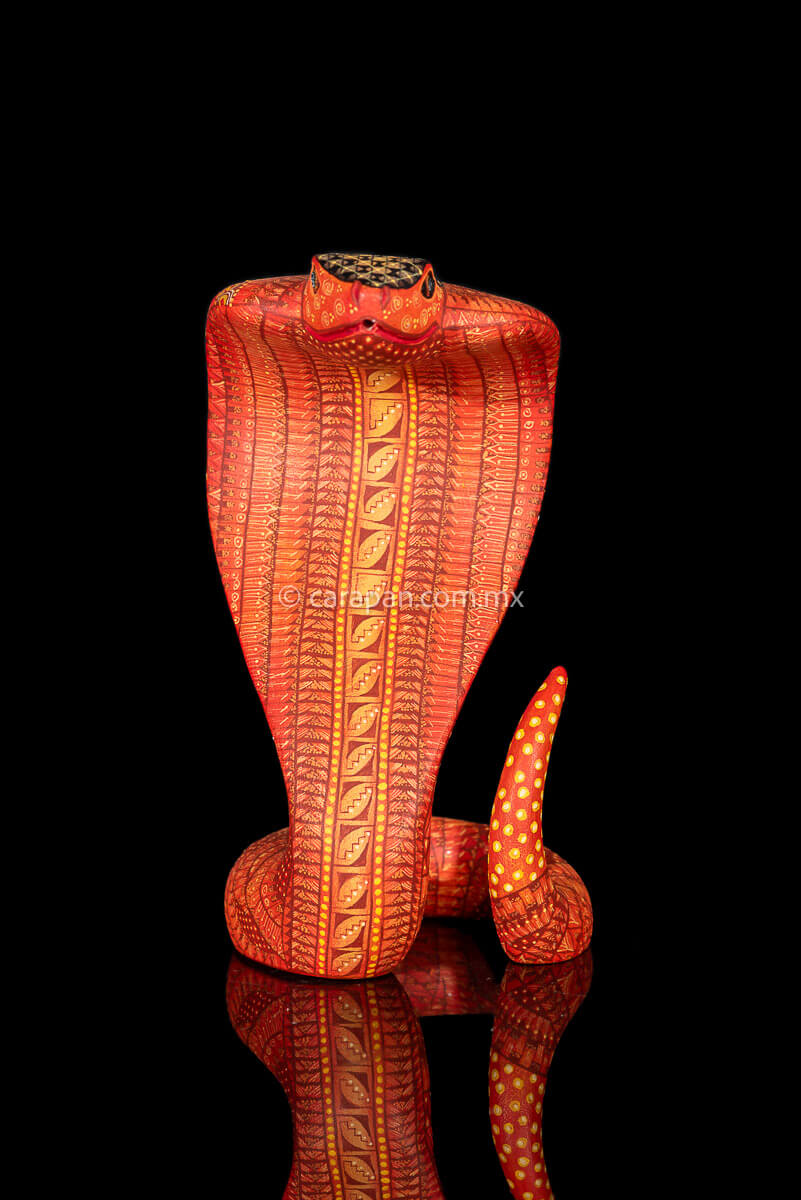 Wooden cobra hand carved from a single block of copal wood in Oaxaca Mexico, decorated with a fine pattern of zapotec symbols in a predominant orange tone 