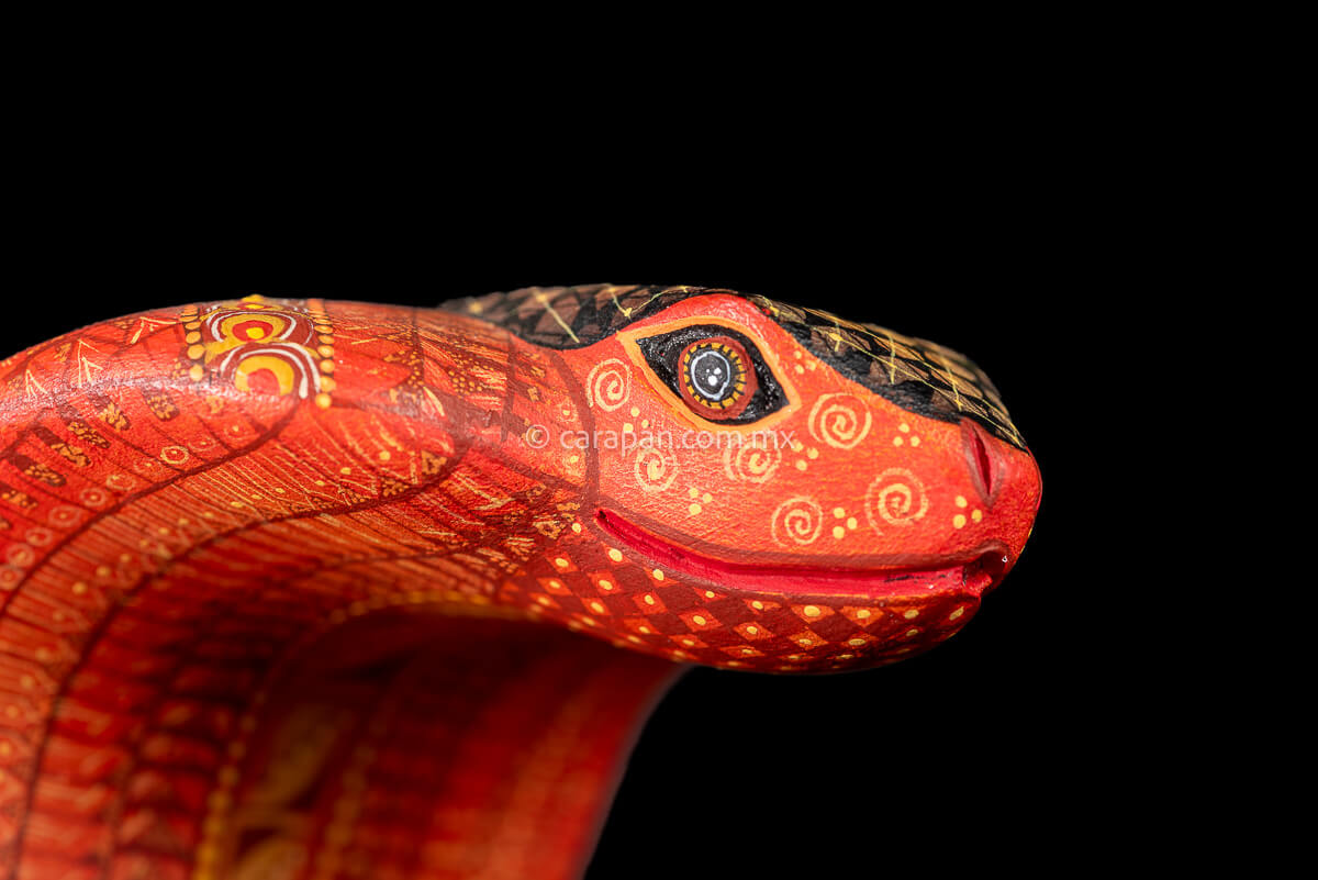 Wooden cobra hand carved from a single block of copal wood in Oaxaca Mexico, decorated with a fine pattern of zapotec symbols in a predominant orange tone 