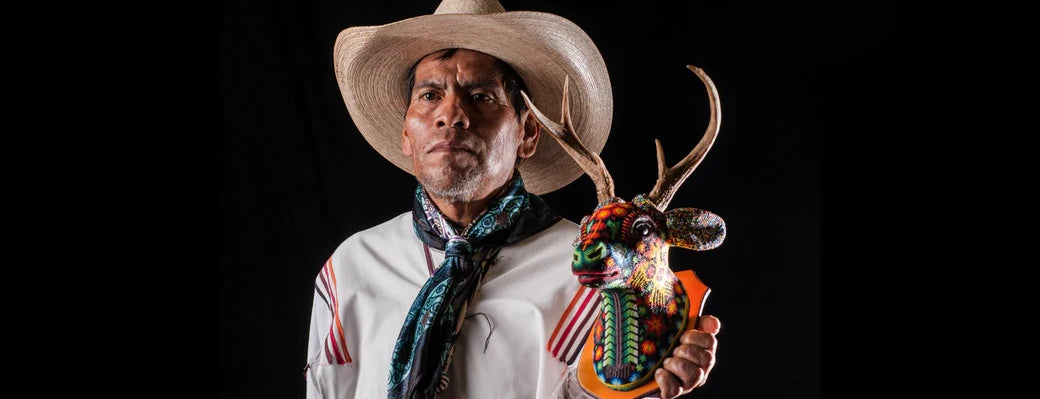 Huichol indigenous artist holding deer head of beaded art. 