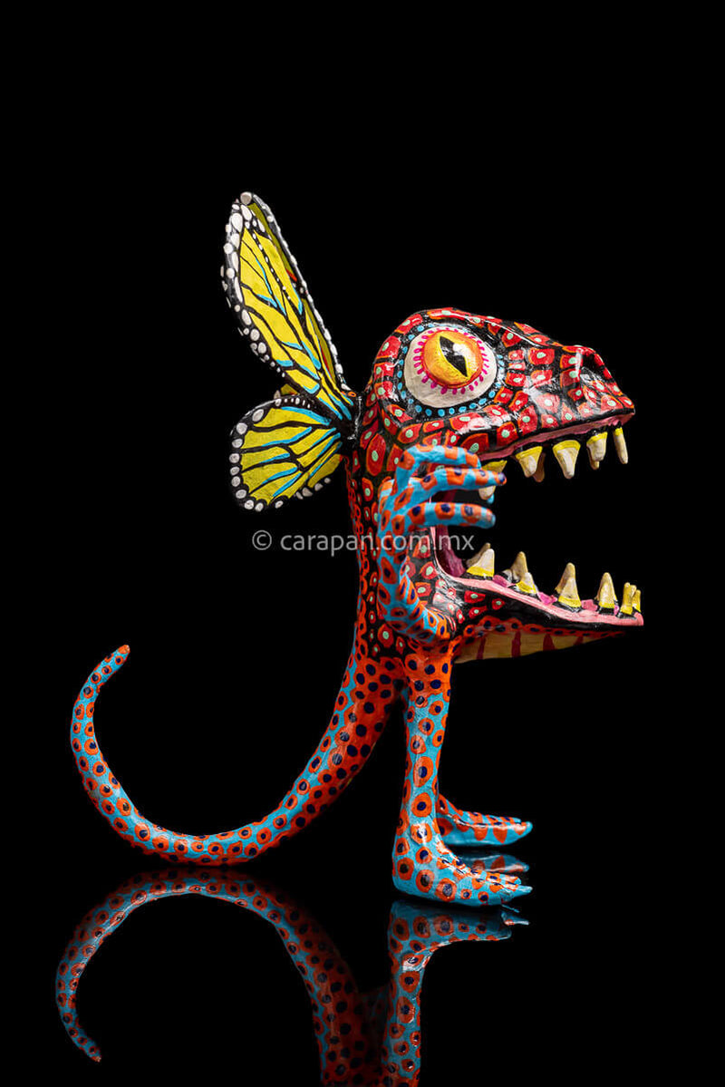 Paper Mache Alebrije with yellow butterfly wings, mouth open showing teeth in fierce expression, big eyes red body & blue legs & Arms decorated with red  patches and blue dots