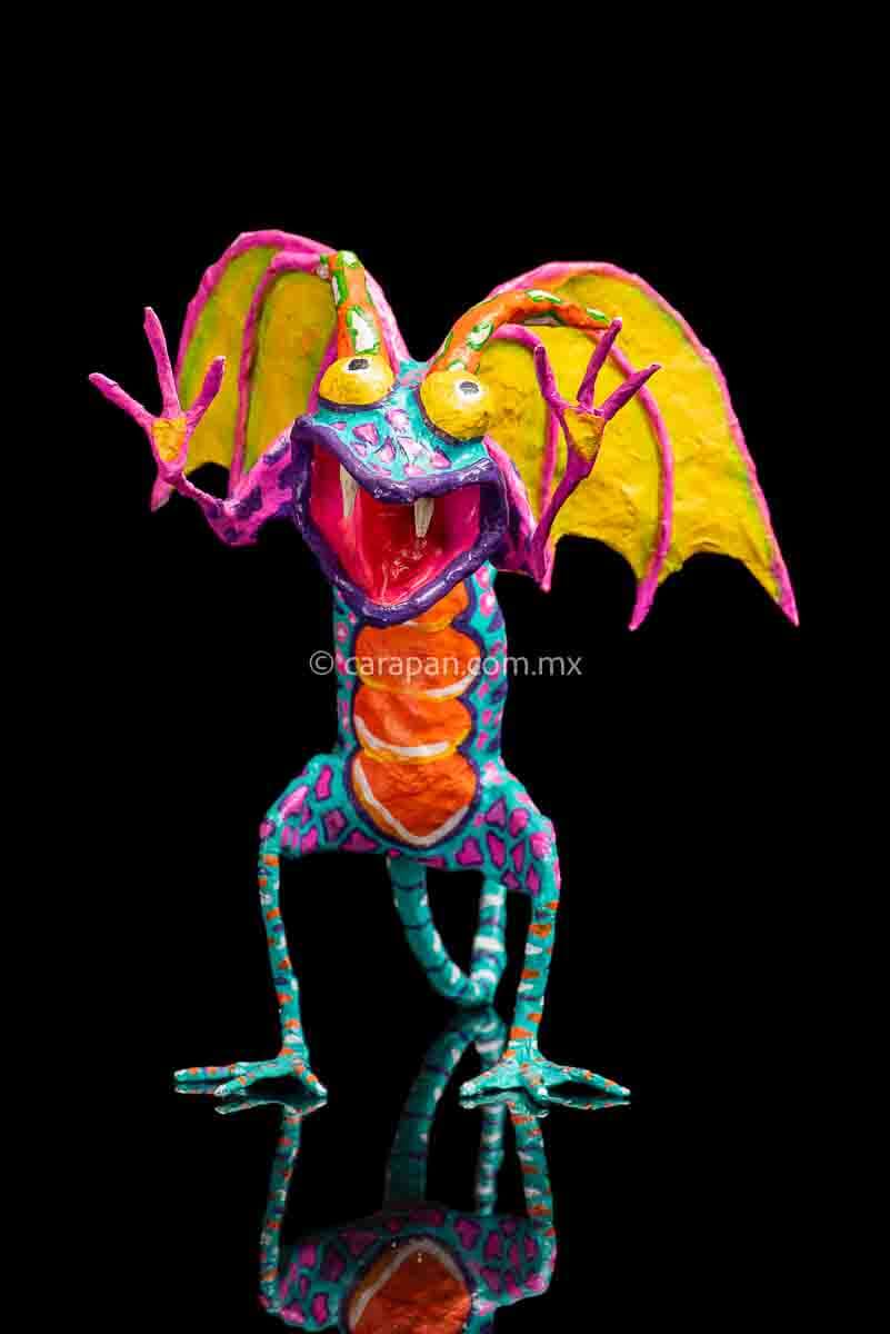 User  Please create a selling description for Paper Mache Alebrije Dragon Style Standing with hands up and mouth open showing 2 fangs popping yellow eyes and two orange horns. His body is painted in turquoise with pink dots and blue stripes and his wings are yellow outlined in pink