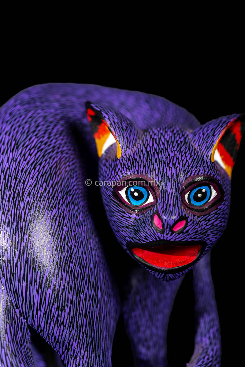Face of Mexican Wooden Sculpture of a purple cat looking backwards with delicate black strokes that resemble fur carved from a single block of wood