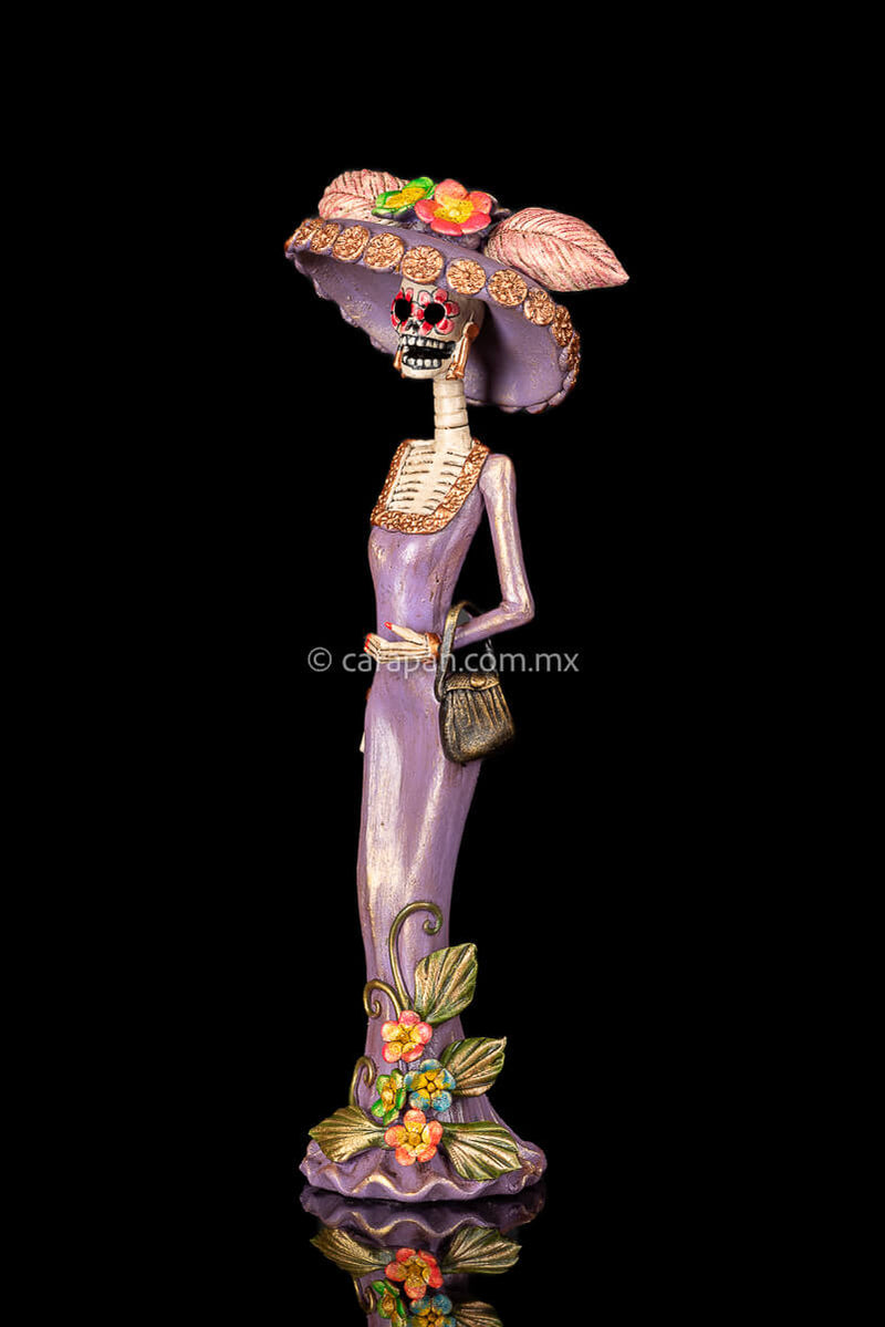 Day of the dead Sculpture, Catrina wearing a purple dress with flowers at the bottom and a traditional Posada Style hat. Crafted in Capula Michoacan Mexico