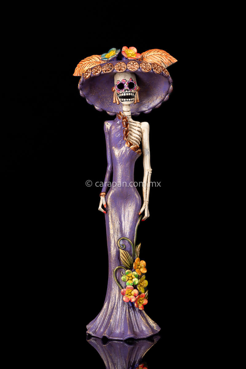 Clay Sculpture of Mexican Catrina, Day of the dead icon inspired by Jose guadalupe posada's work wearing a purple dress with one sleeve, decorated with flowers at the bottom and wearing a traditional hat